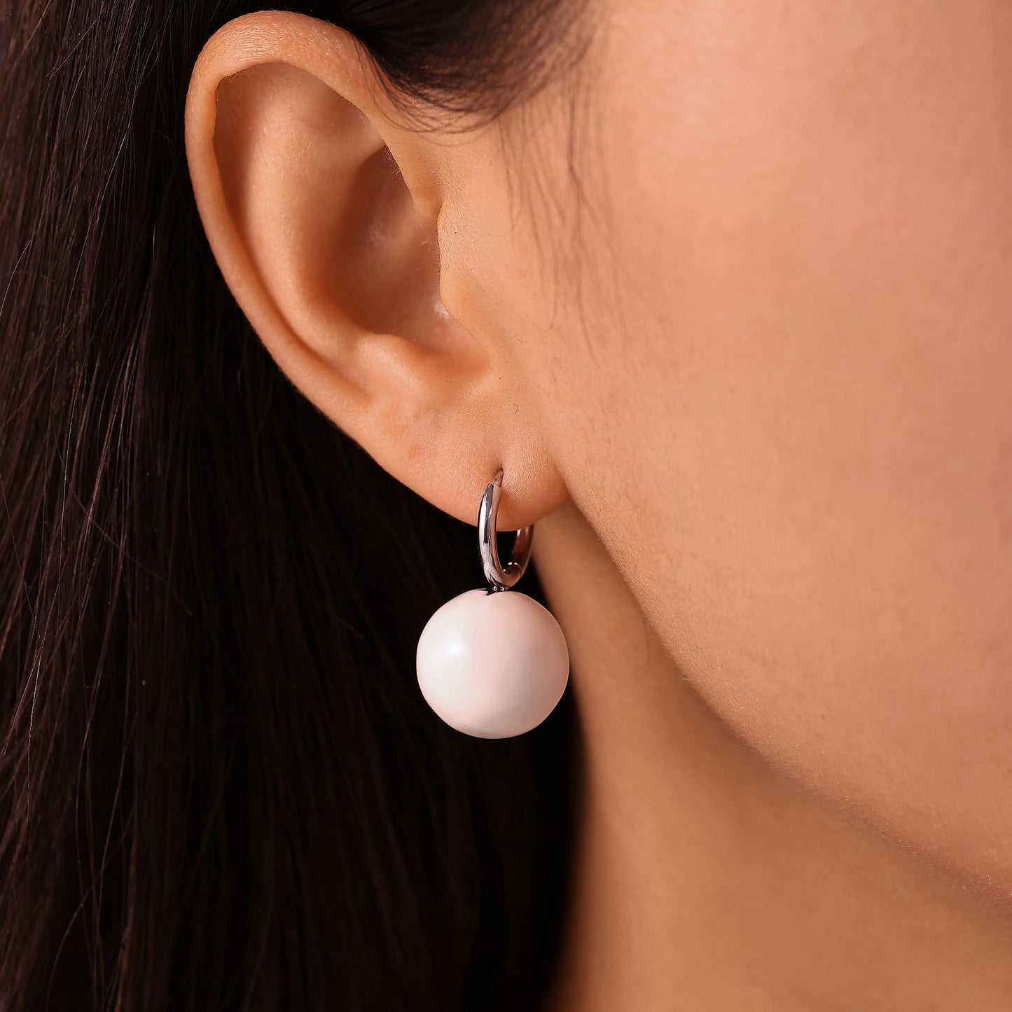 Side view of model wearing a white ball drop earring with a steel-tone hoop