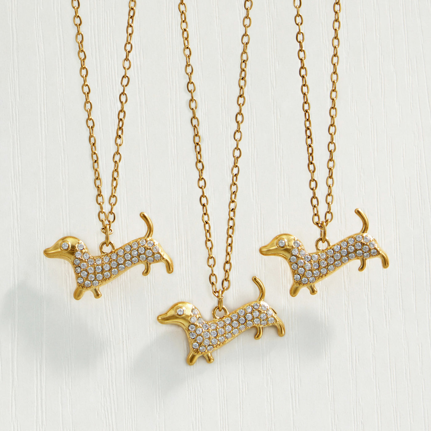 Close-up collection of gold dachshund zircon rings and pendant necklaces on a neutral background