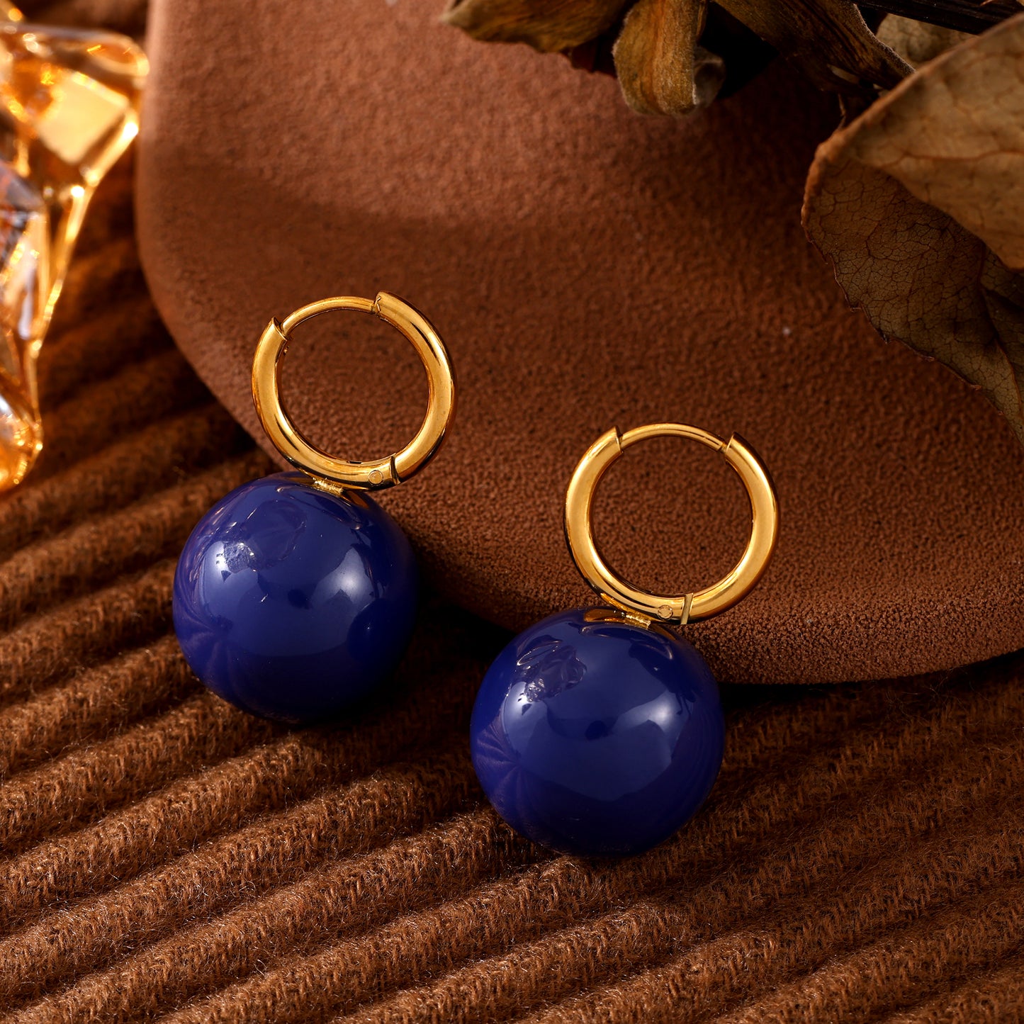 Navy ball drop earrings with gold-tone hoops displayed on a wooden surface