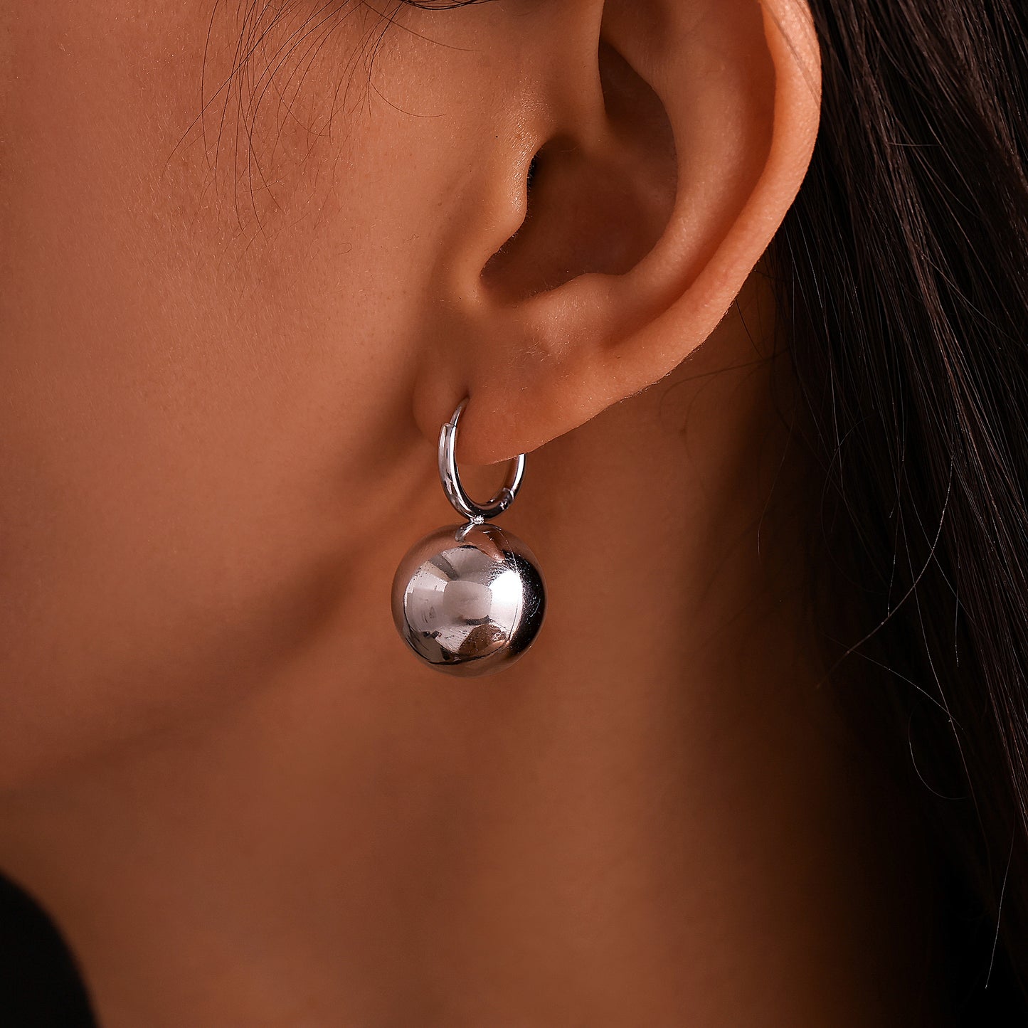Model wearing a silver sphere drop earring with a steel-tone hoop
