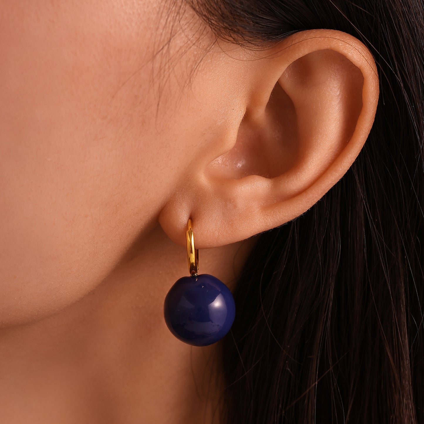 Model wearing navy ball drop earrings with gold-tone hoops