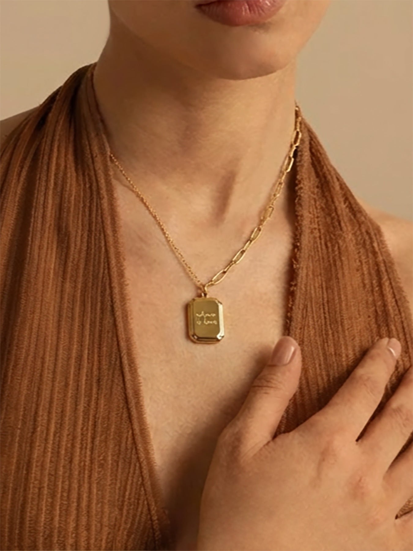 Close-up shot of male model wearing gold plated "where is love" tag necklace, focusing on the engraved pendant and dual chain design