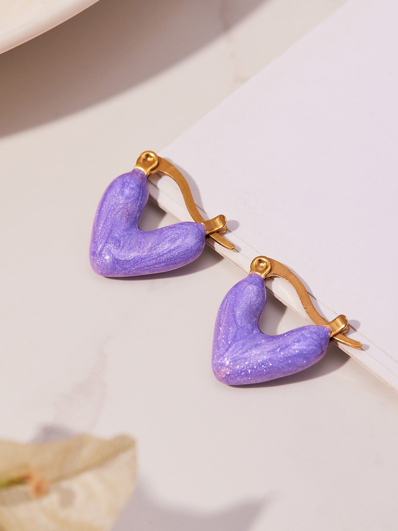 Tarnish-free purple enamel heart huggies made of 316L surgical steel with 18K gold plating.