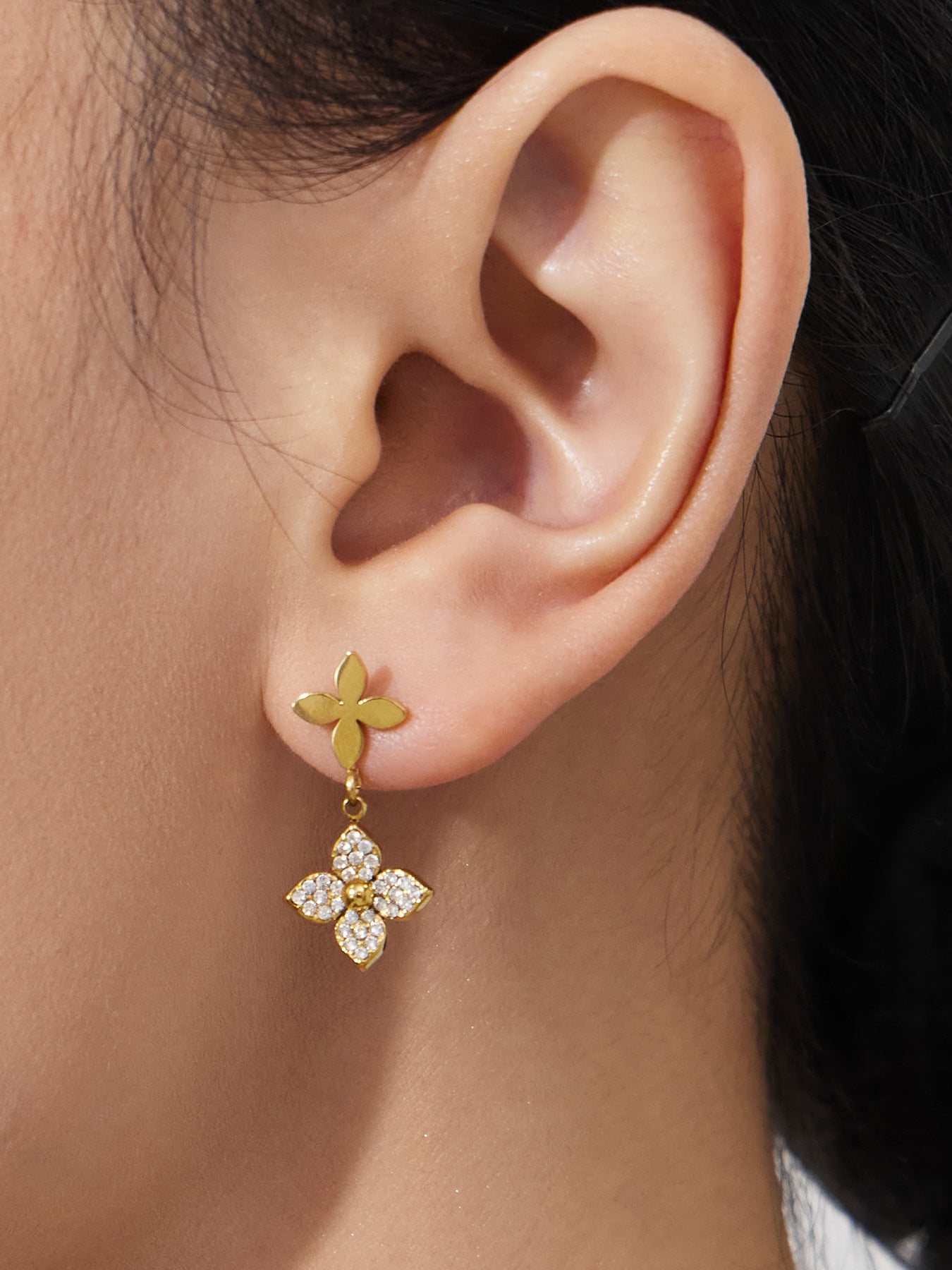 Detail of geometric drop earrings with flower zircon accents worn on the ear, perfect for sensitive skin.