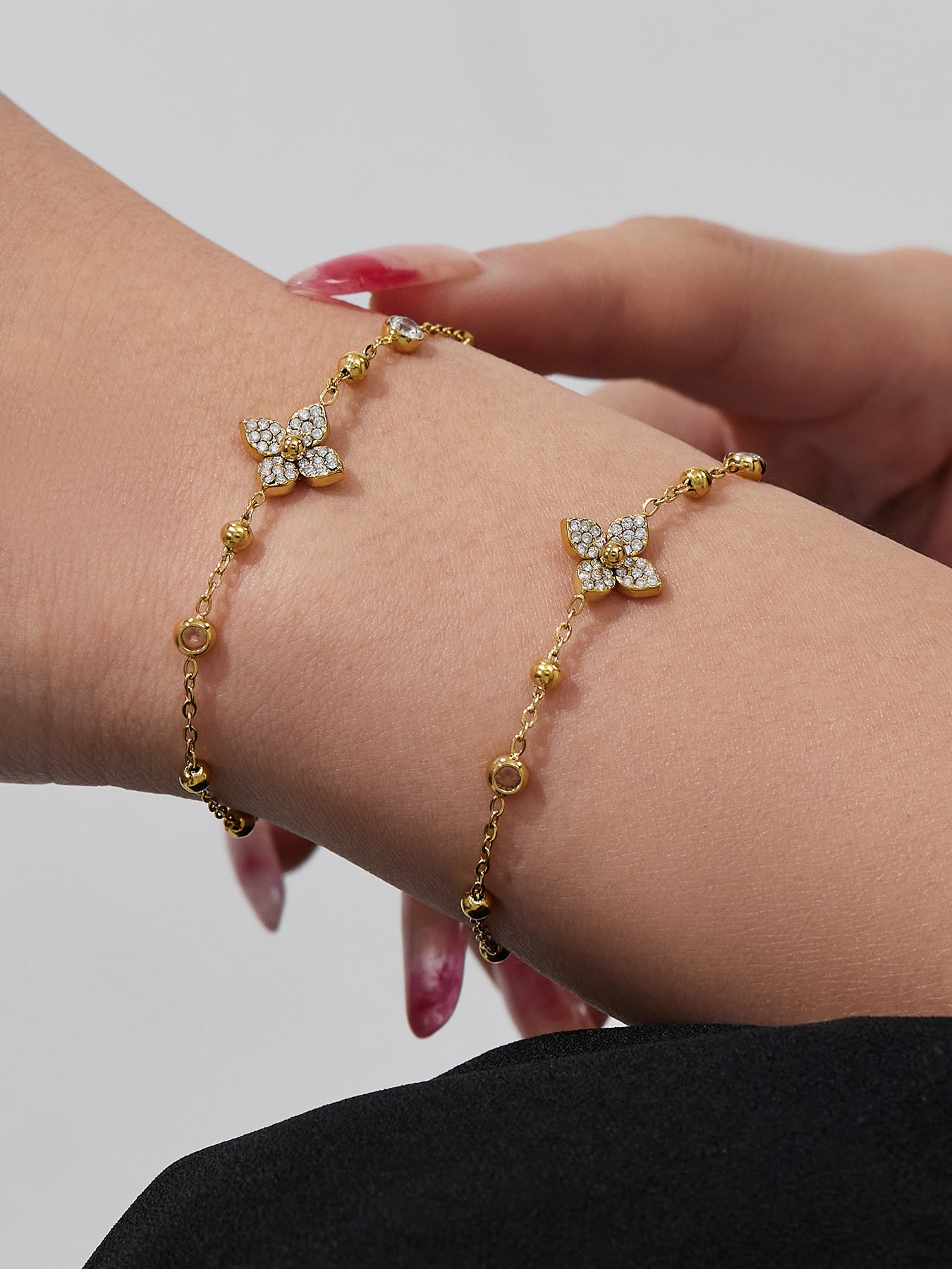 A gold geometric link bracelet with flower zircon charms worn on a woman's wrist, waterproof and tarnish-free.