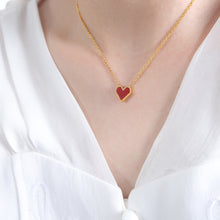 A woman wearing a dainty red heart pendant necklace made of hypoallergenic 316L stainless steel for a romantic look.