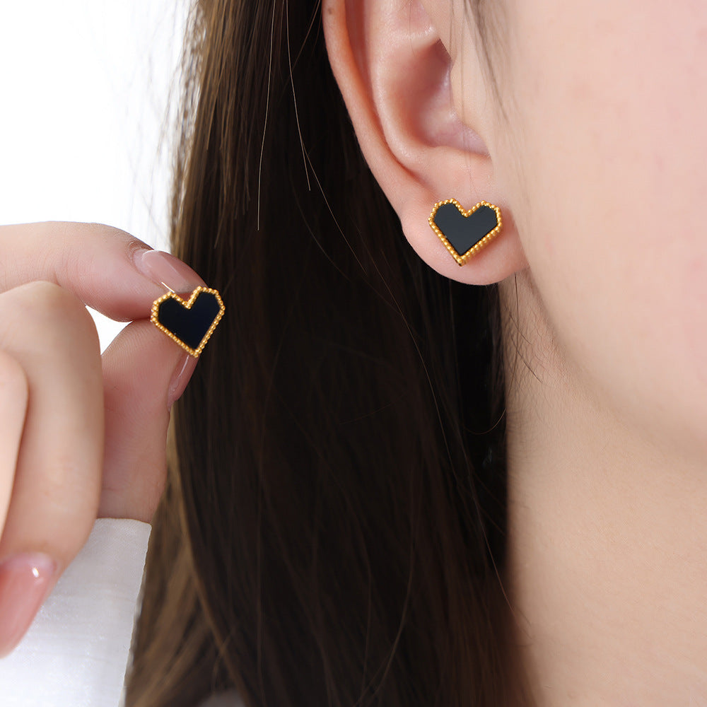 Small black heart stud earrings worn on the ear, crafted from tarnish-resistant 316L stainless steel.