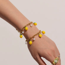 A dainty gold link bracelet with yellow lemon pendants and shell pearls worn on a woman's wrist, perfect for sensitive skin.