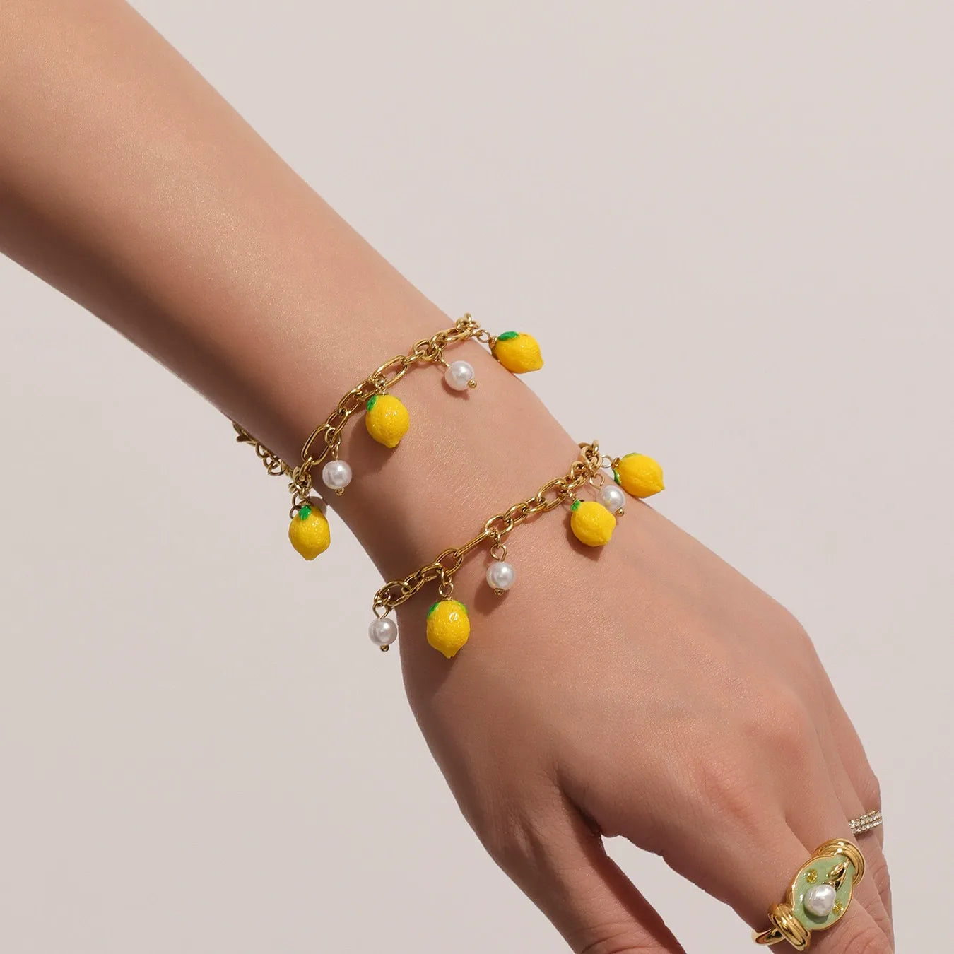 A dainty gold link bracelet with yellow lemon pendants and shell pearls worn on a woman's wrist, perfect for sensitive skin.