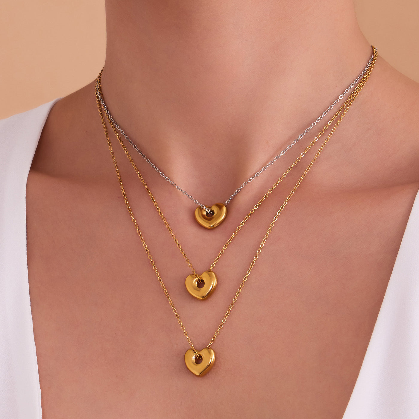 Detailed view of two layered gold puffed heart pendants on a woman's neck, perfect for sensitive skin.