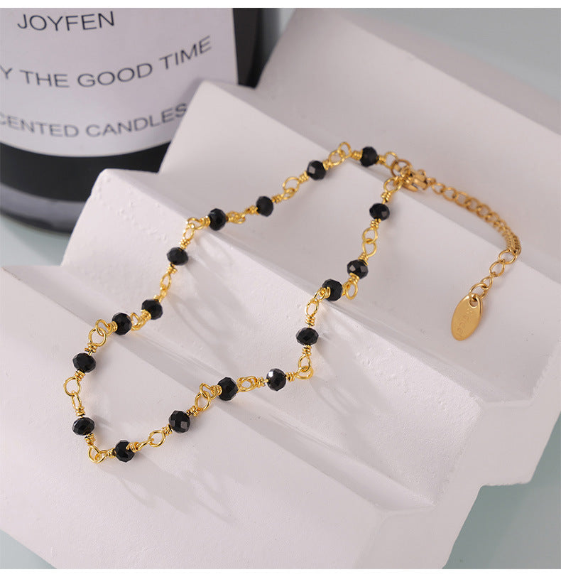 Neutral studio shot of black and gold beaded anklet laid flat on white fabric, minimalist handmade design for boutique display