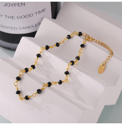 Neutral studio shot of black and gold beaded anklet laid flat on white fabric, minimalist handmade design for boutique display