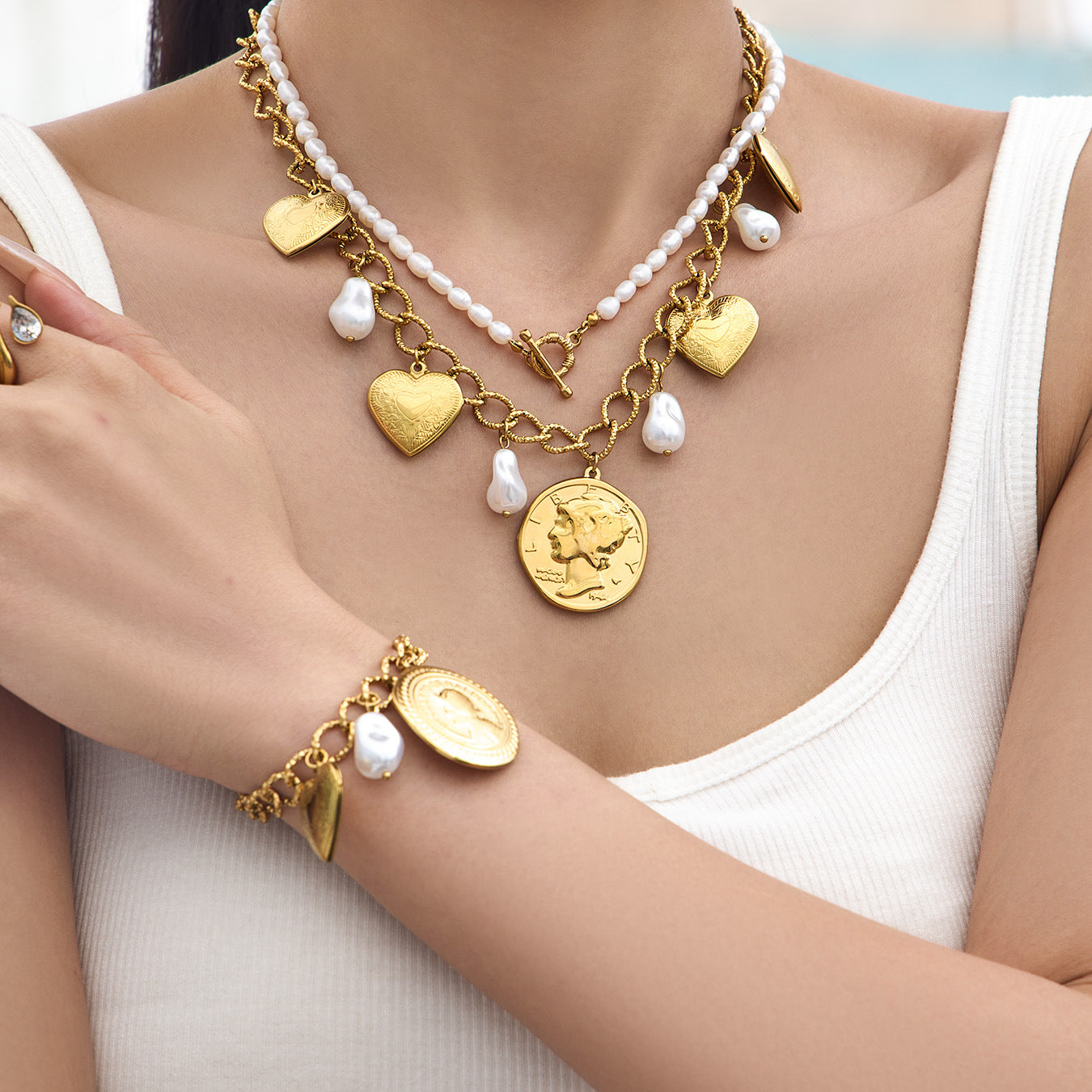 model wearing layered gold heart charm necklace with pearl accents
