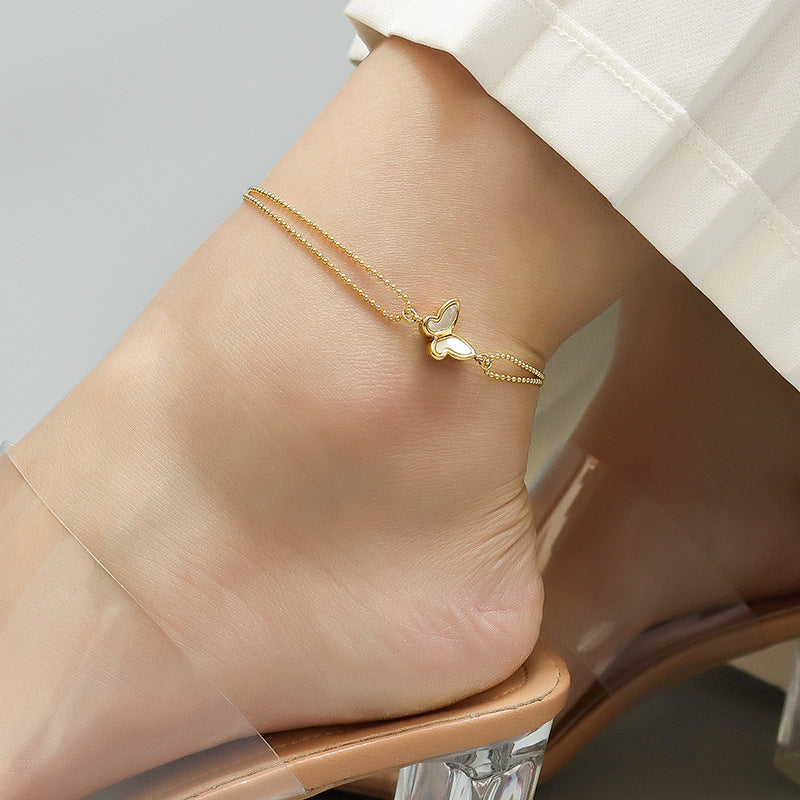 Layered gold stainless steel anklets with butterfly and heart charms on a woman's ankle, dainty minimalist summer styling for boutique display