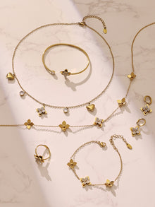 Aesthetic flat lay of the four-petal flower jewelry collection including matching bracelets and necklaces in a rich gold tone.