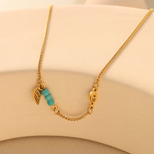Delicate gold turquoise wing anklet flat lay on neutral background, 316L stainless steel construction and PVD gold plating for sensitive skin