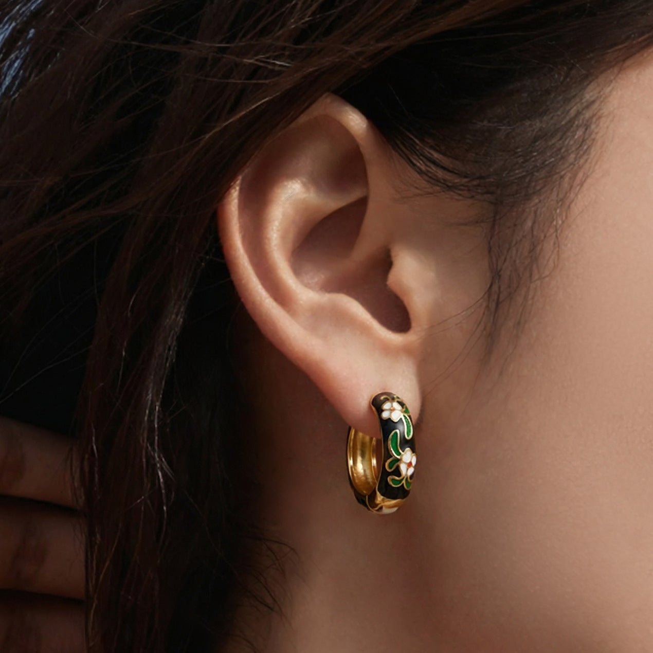 Model wearing black enamel floral hoop earrings with gold tone stainless steel finish.