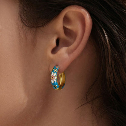 Model wearing blue enamel floral hoop earrings with gold tone stainless steel finish.