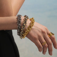 Two-tone 316L stainless steel heart charm bracelet held by model near beach background