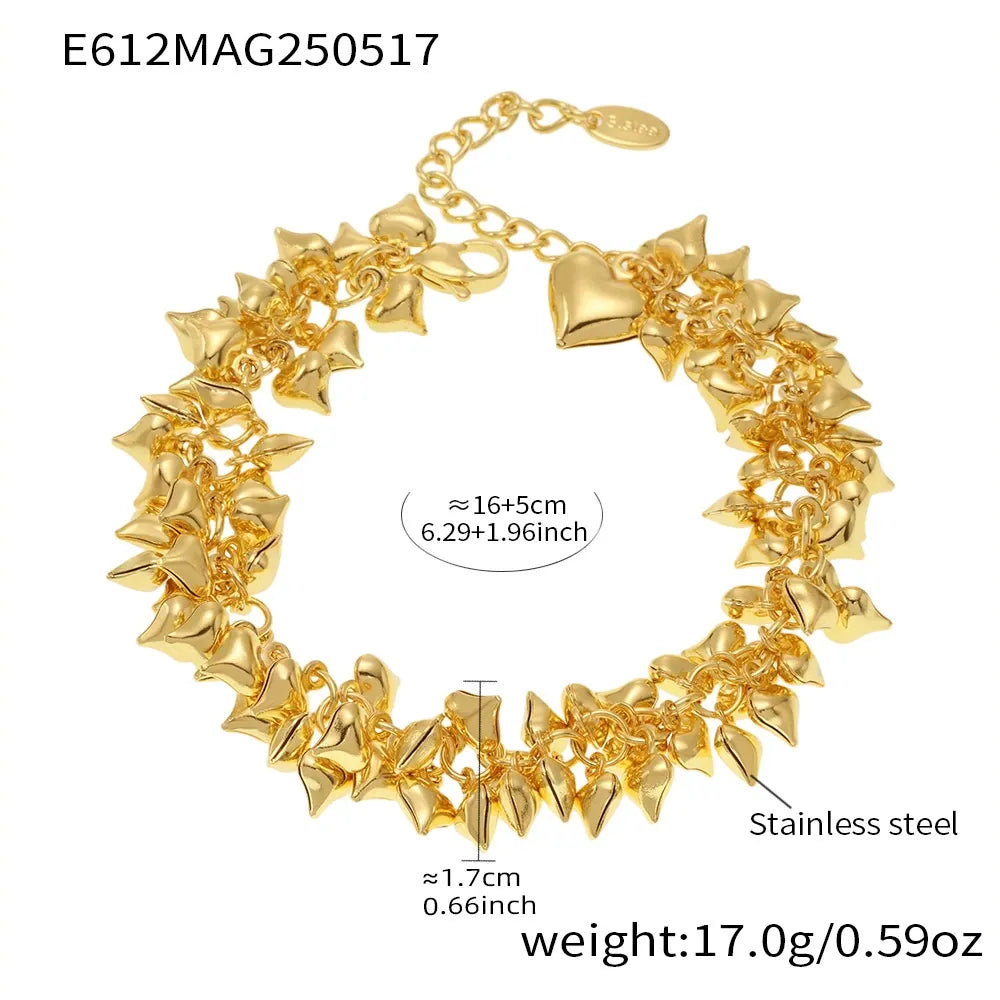 Stacked chunky heart charm bracelets in gold and steel styled on wrist by the beach