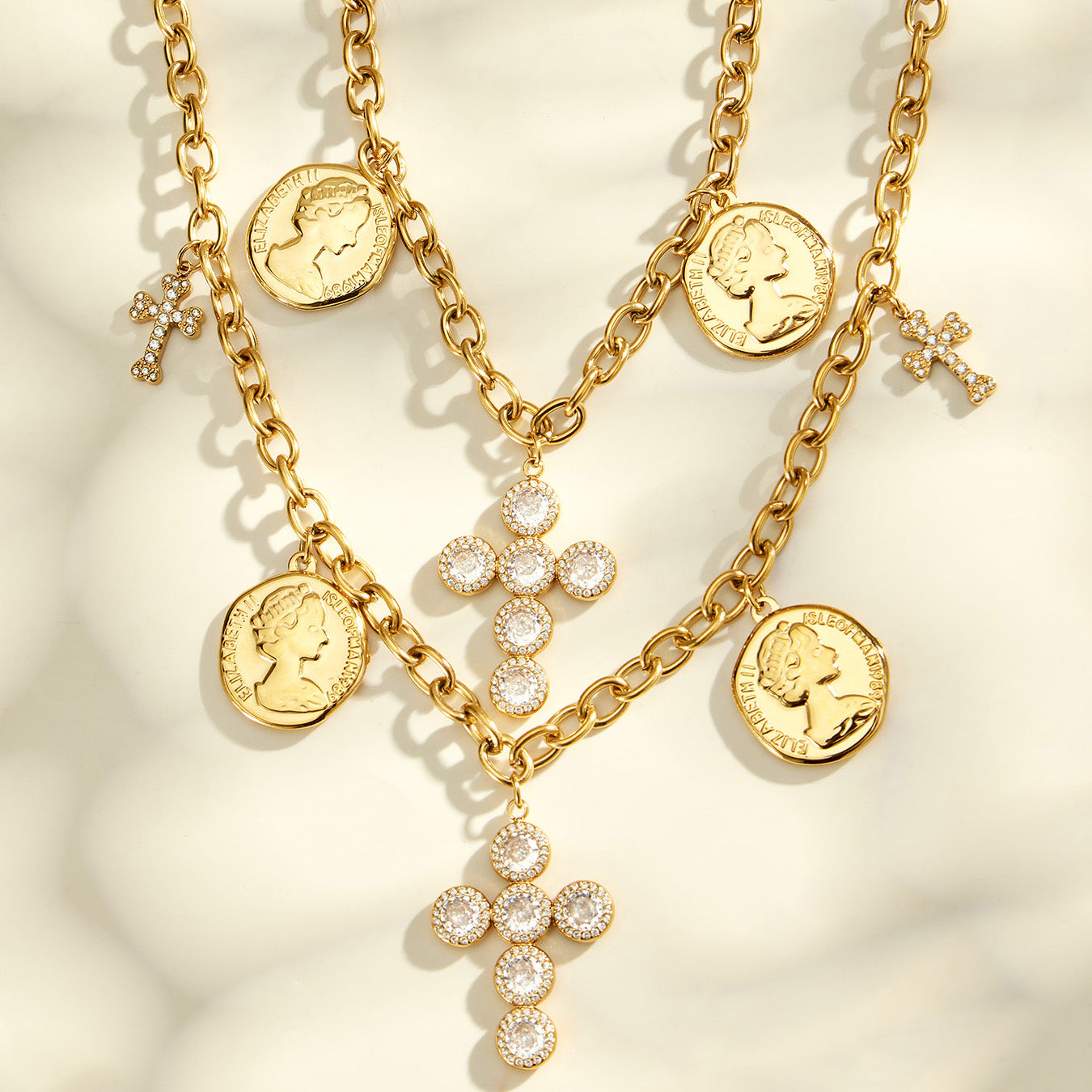 Layered gold-tone necklaces with coin pendants and cross charms arranged on a cream surface