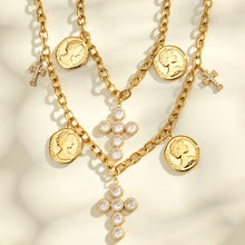 Layered gold-tone necklaces with coin pendants and cross charms arranged on a cream surface