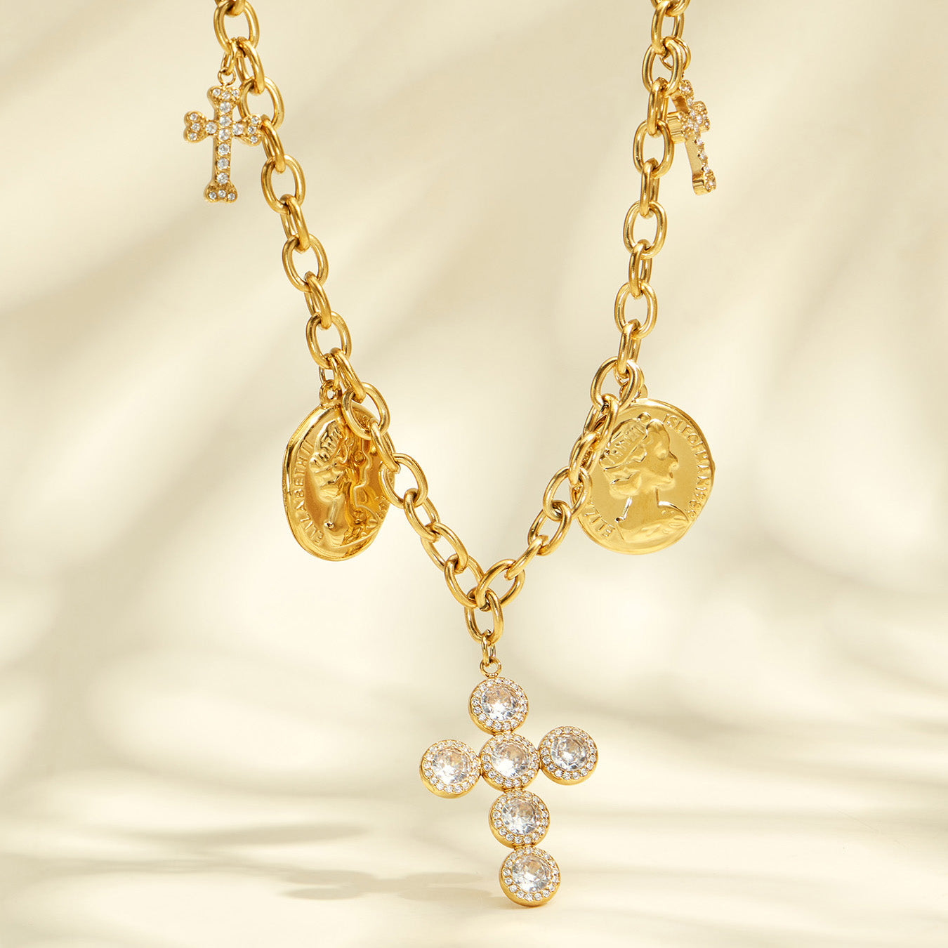 Close-up of a clear zircon cross pendant and engraved coin charms on gold-tone chains