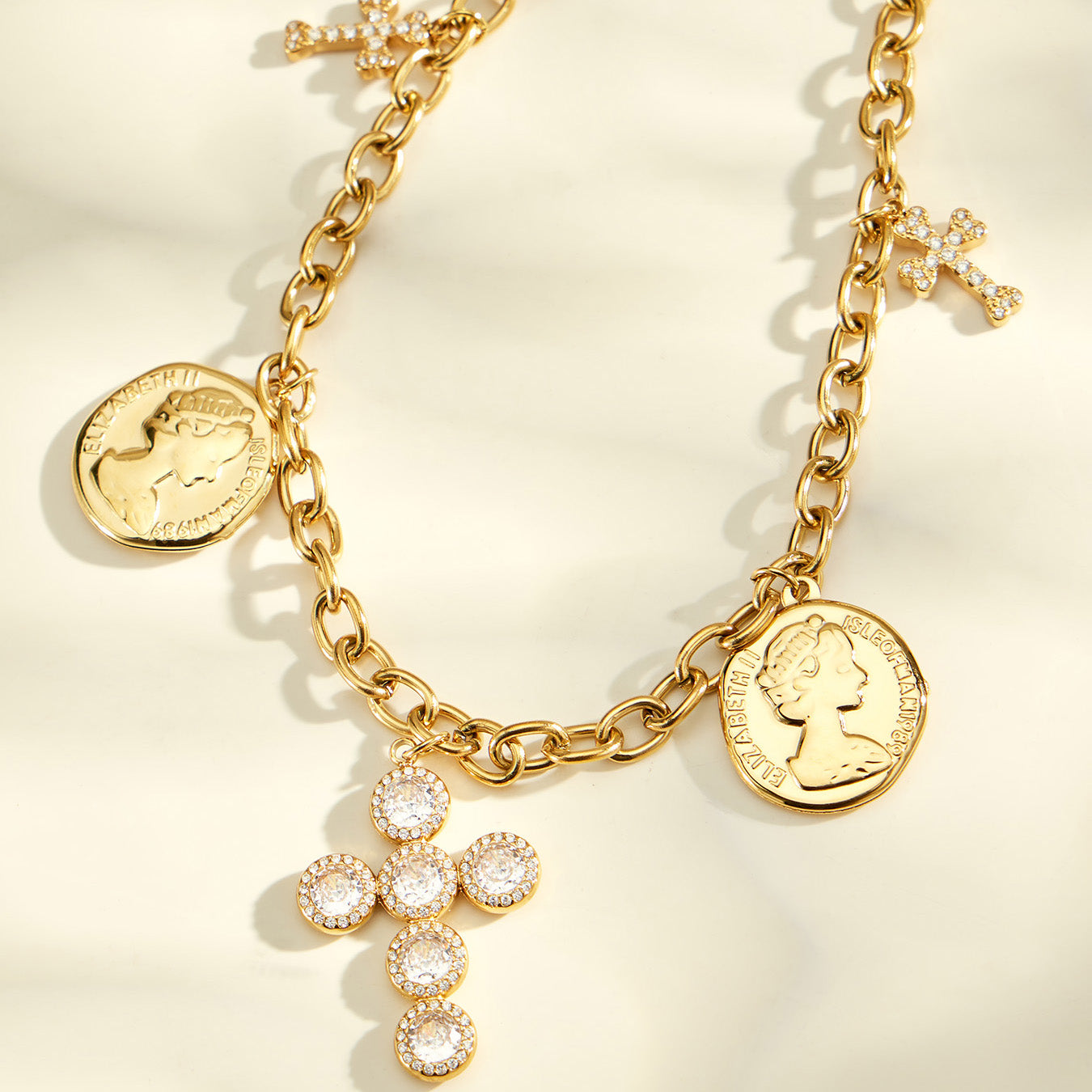 Close-up of a gold-tone cross necklace with two coin pendants and small side charms
