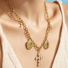 Close-up of layered gold-tone necklaces with coin charms and a clear zircon cross pendant