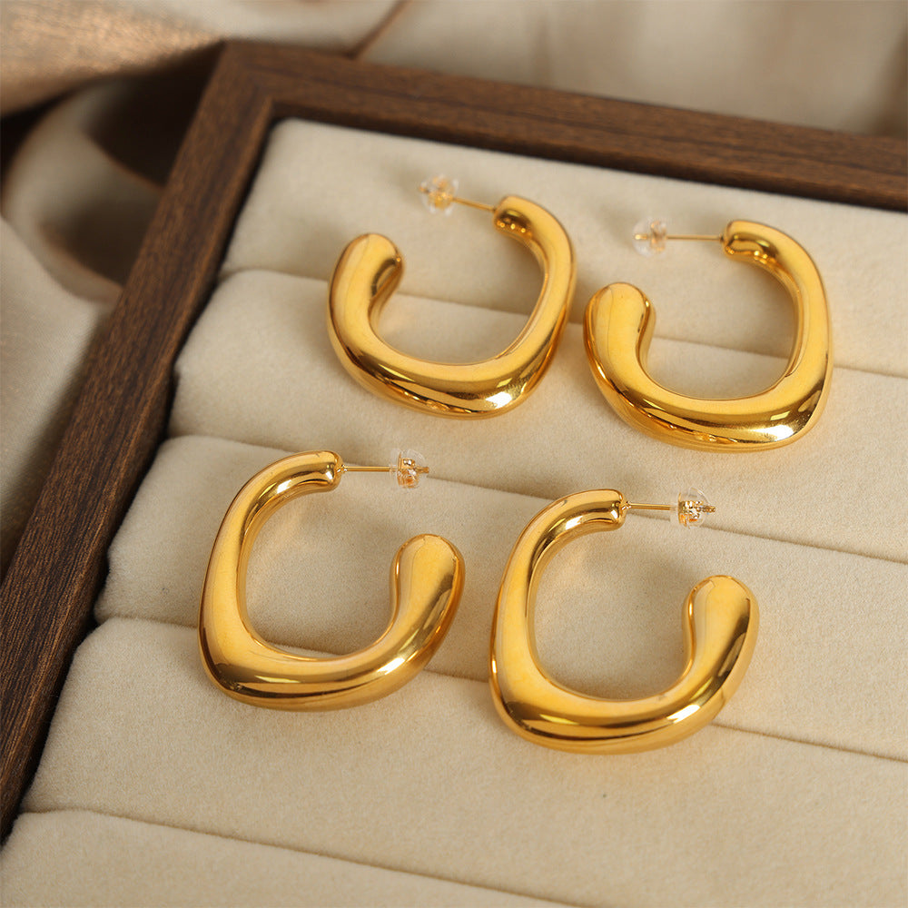 Model wearing 316L stainless steel geometric G-shaped hoop earrings with polished gold PVD finish