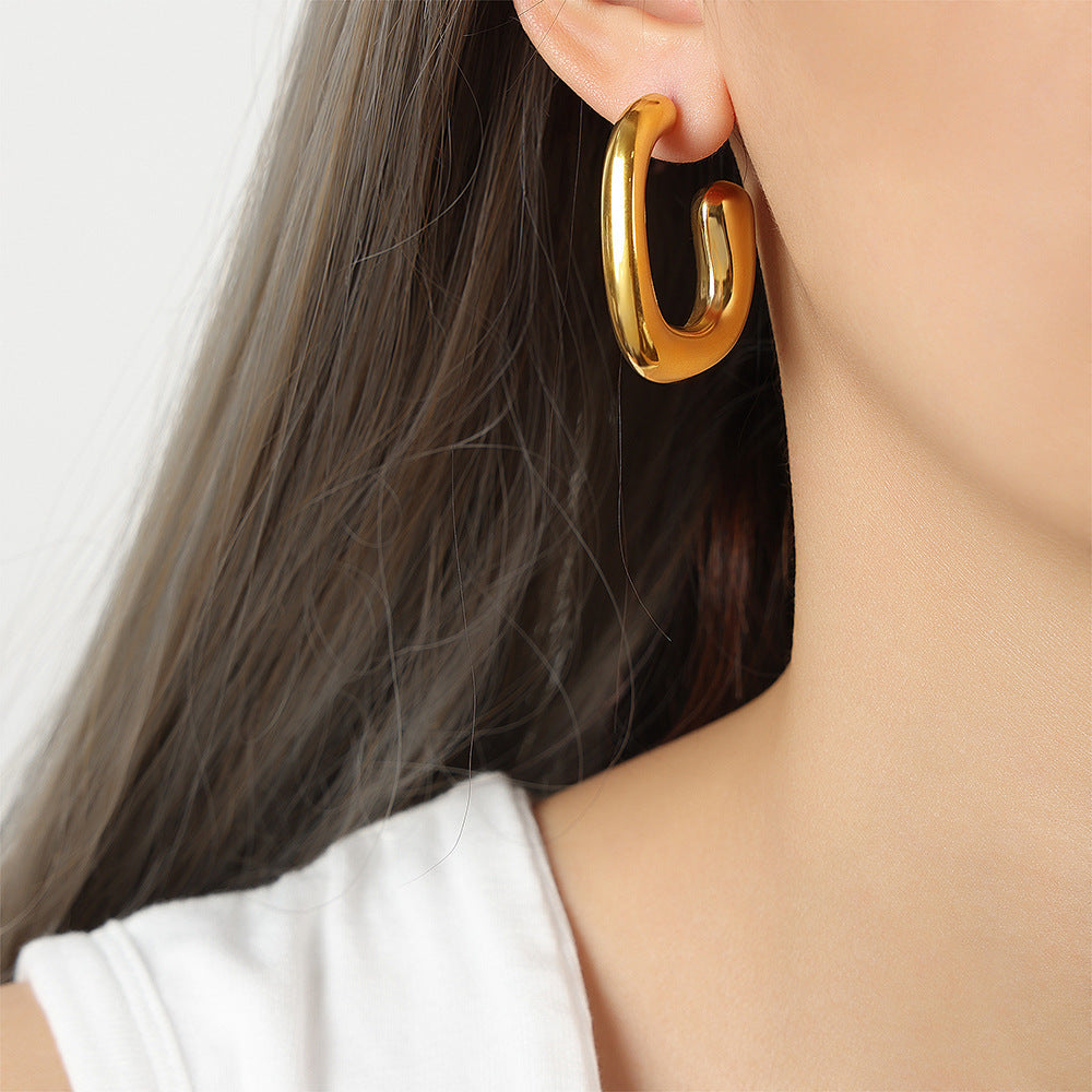 Model wearing 316L stainless steel geometric G-shaped hoop earrings with polished gold PVD finish