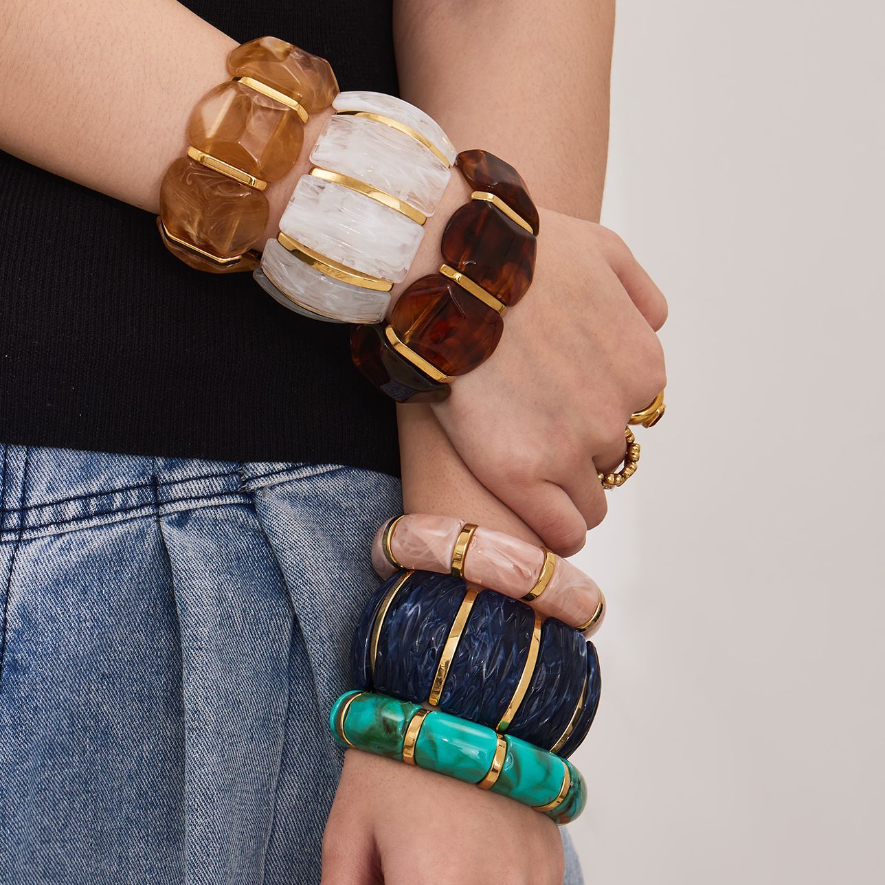 Model wearing stacked wide resin stretch bracelets with gold stainless steel accents in multiple colors