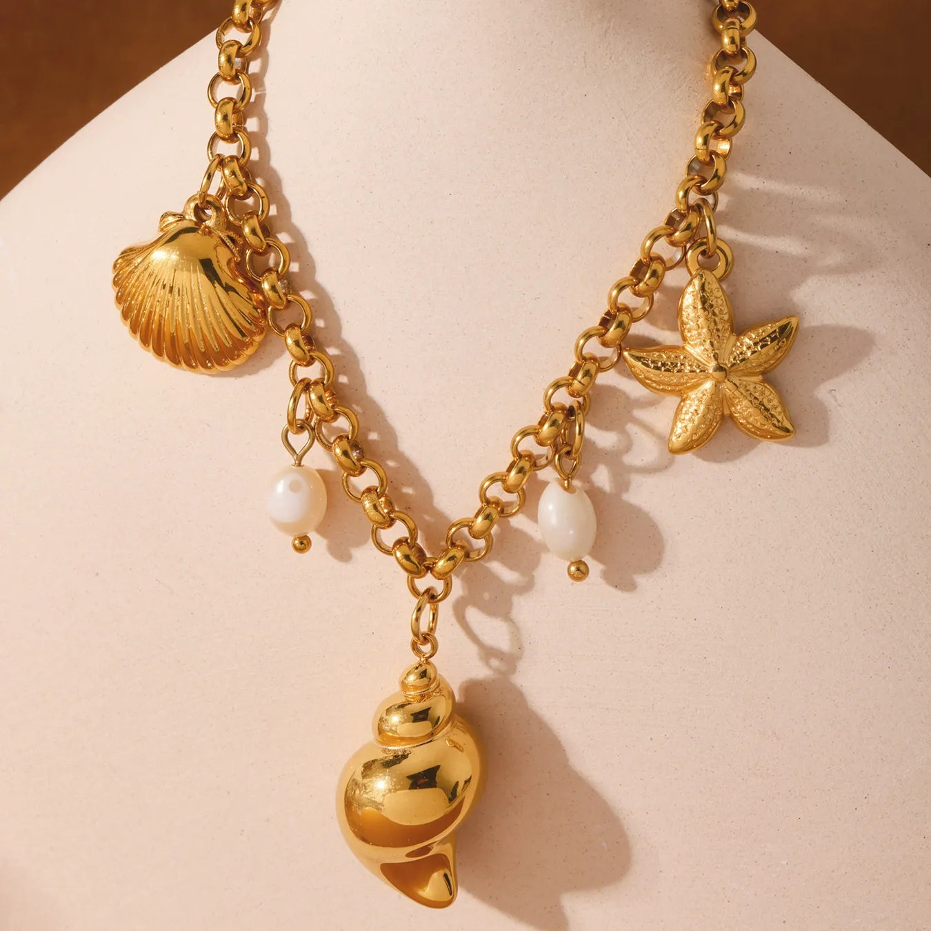 Close-up of gold conch shell freshwater pearl and starfish charm anklet on warm towel, waterproof stainless steel beach jewelry