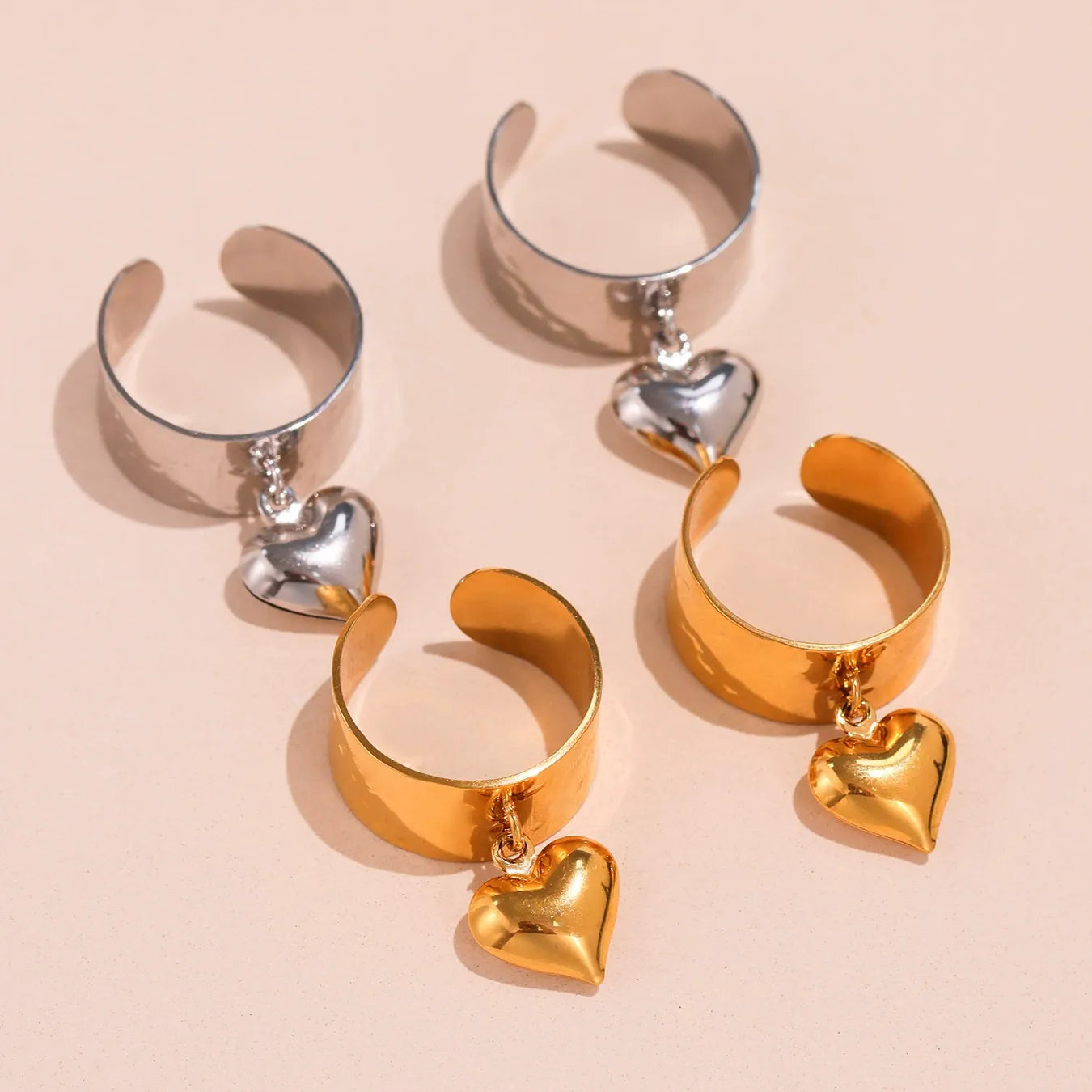 A pair of gold and silver waterproof wide band dangle heart rings displayed side by side.