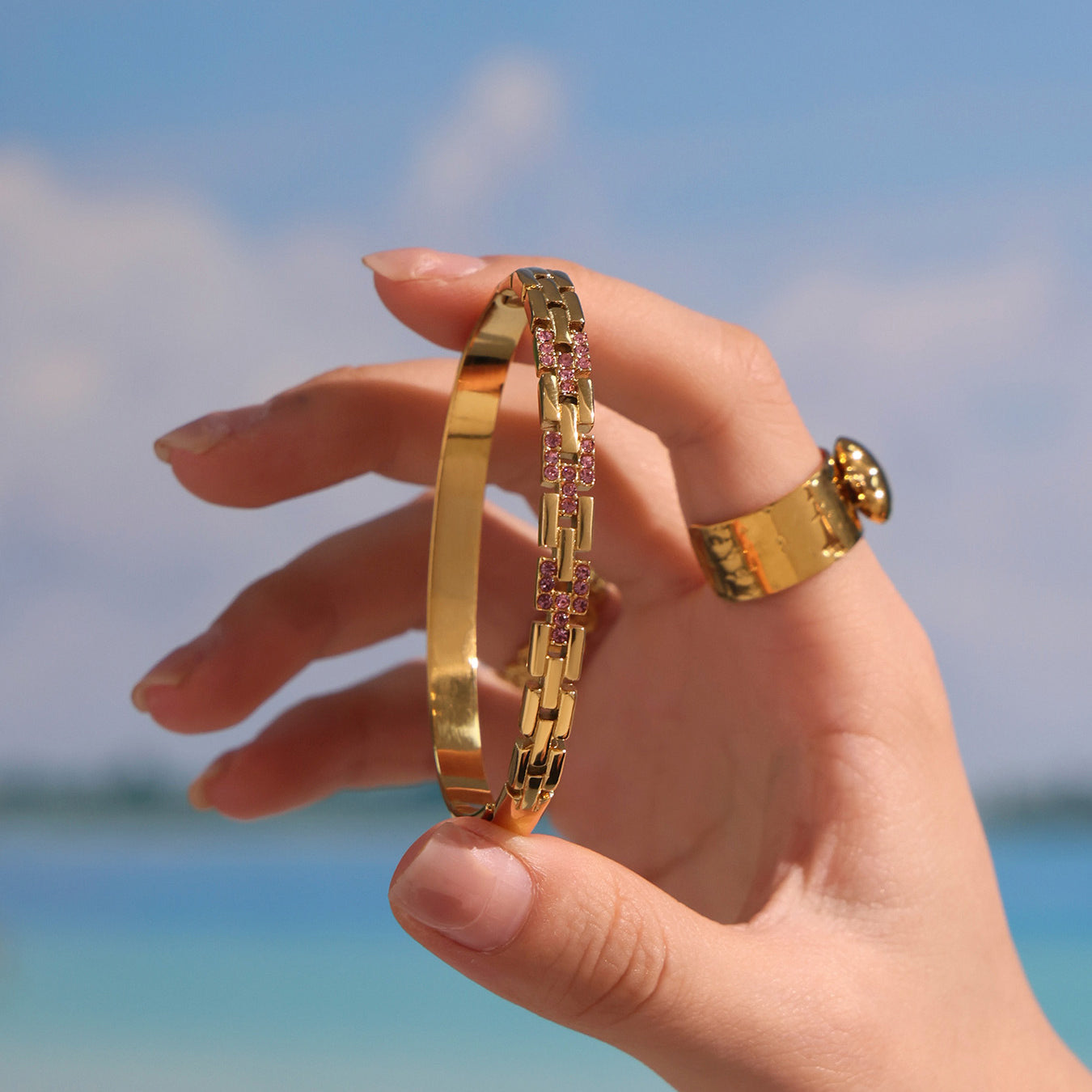 18k gold plated 5a zircon clasp bangle, held in hand against beach background