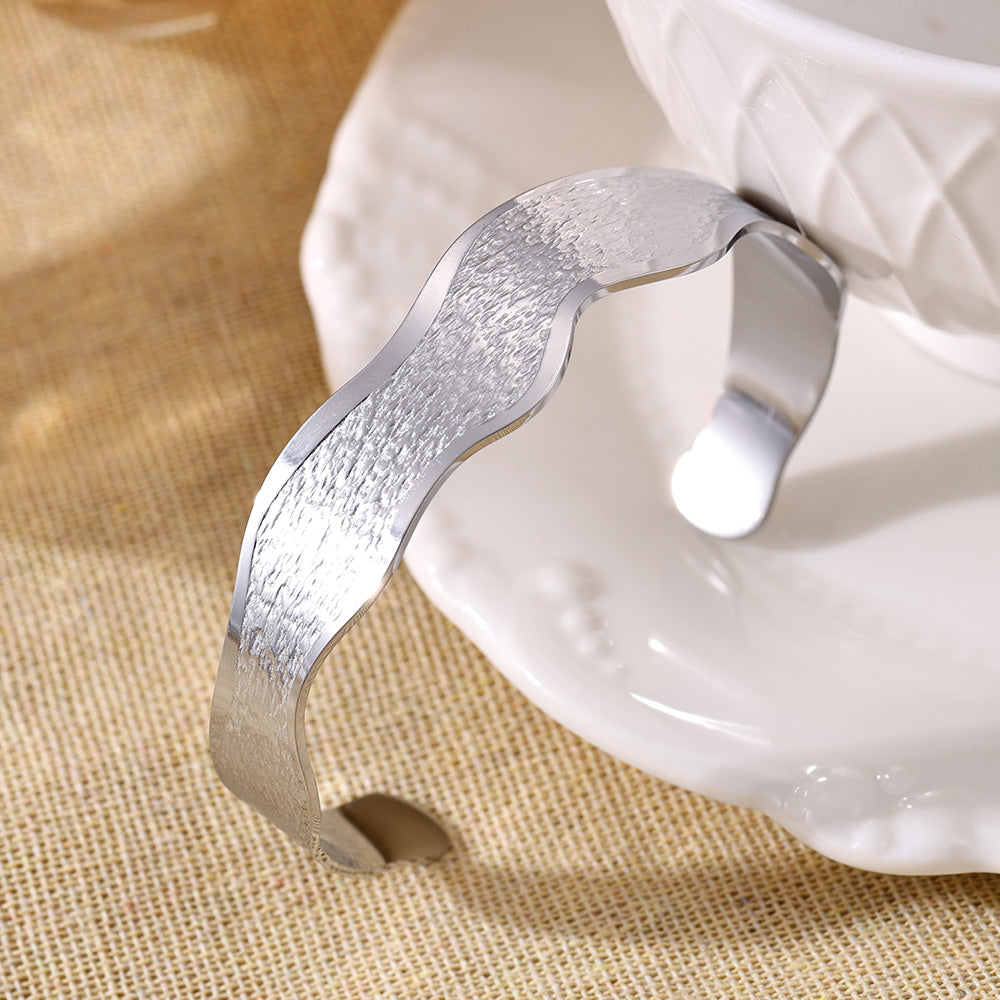 Silver wave texture open bangle displayed on white dish, elegant minimalist jewelry