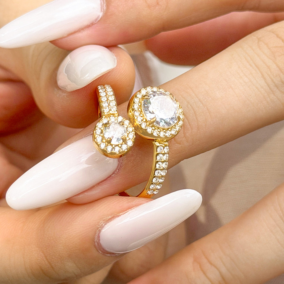 Close-up of a gold-tone stainless steel double halo ring on a finger, showing the two round cubic zirconia settings
