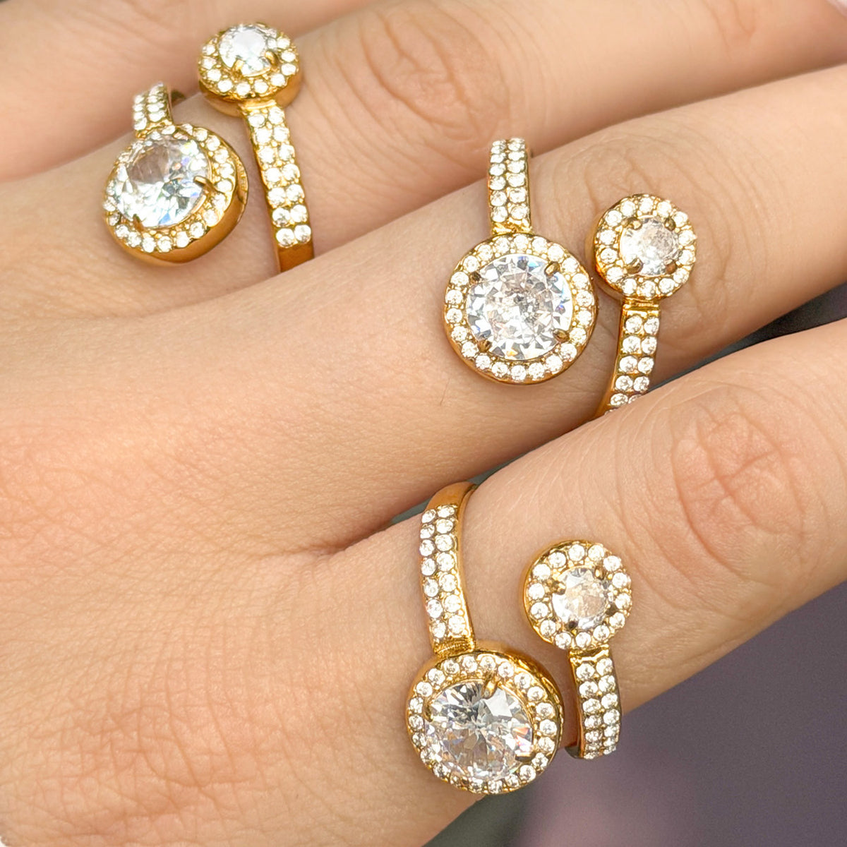 Close-up of three gold-tone stainless steel double halo rings, highlighting the small stones along the curved bands