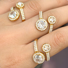 Close-up of three gold-tone stainless steel double halo rings, highlighting the small stones along the curved bands