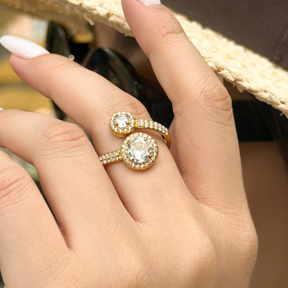 Gold-tone stainless steel double halo ring worn on a finger, showing two raised round cubic zirconia settings