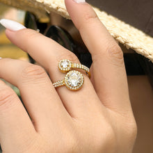Gold-tone stainless steel double halo ring worn on a finger, showing two raised round cubic zirconia settings