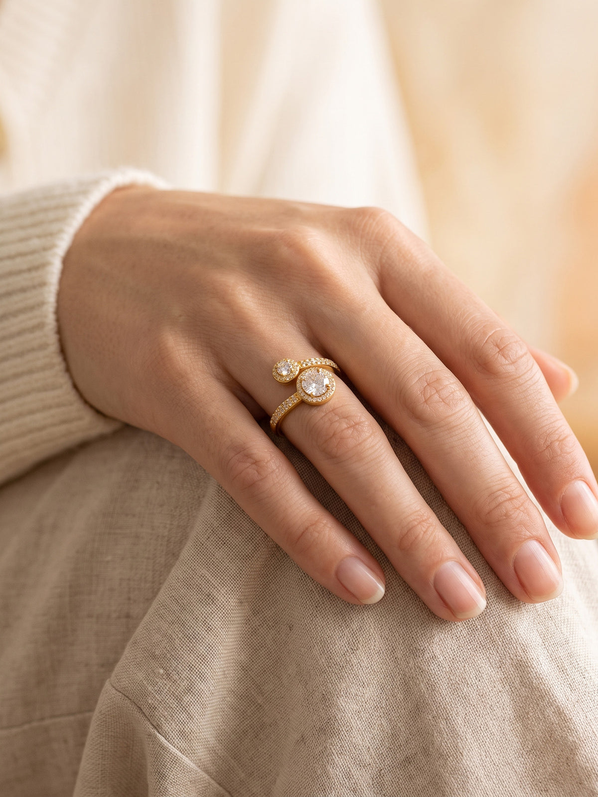 Gold-tone stainless steel double halo ring worn on a model's hand resting against a beige outfit