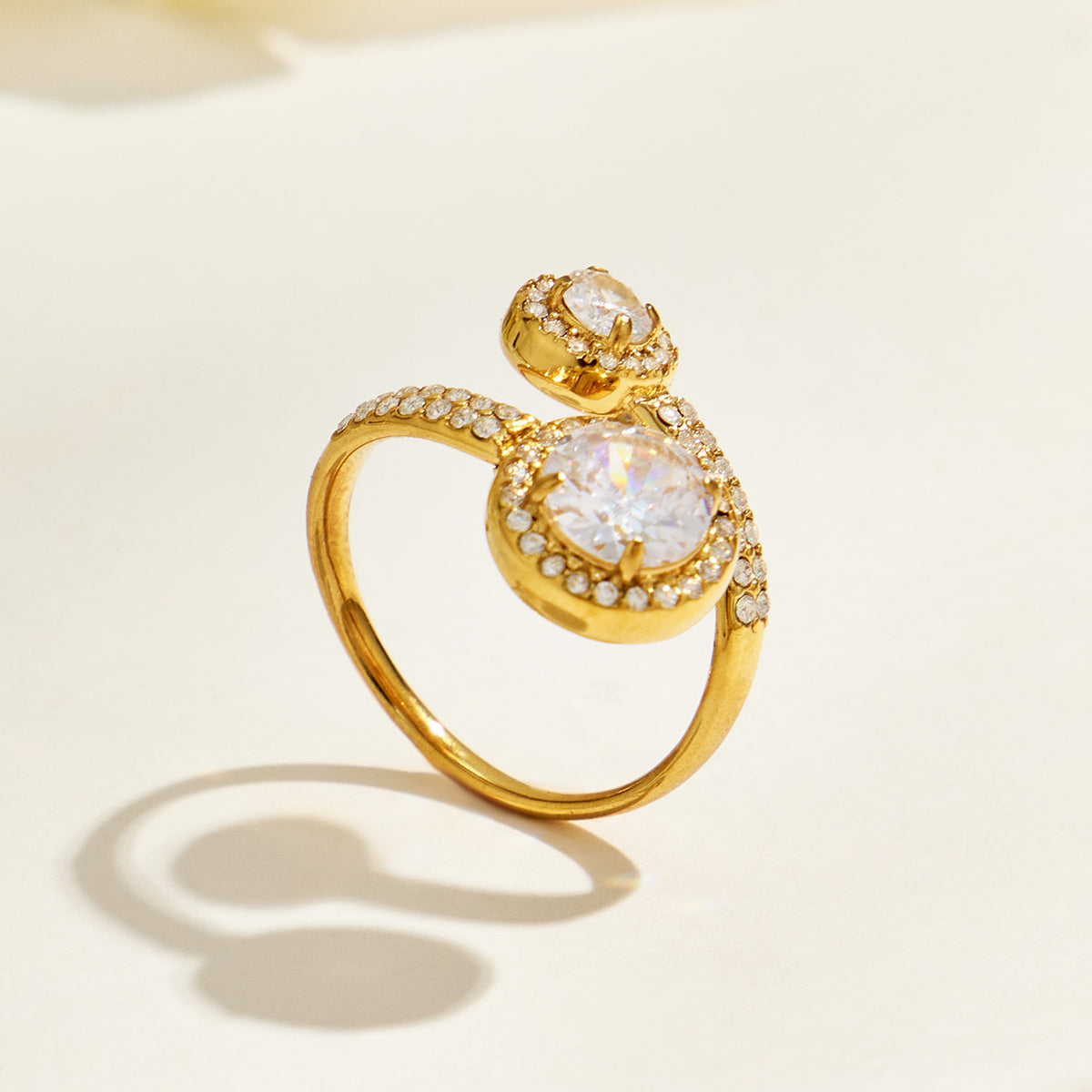 Gold-tone stainless steel double halo ring standing upright on a cream surface and casting a curved shadow