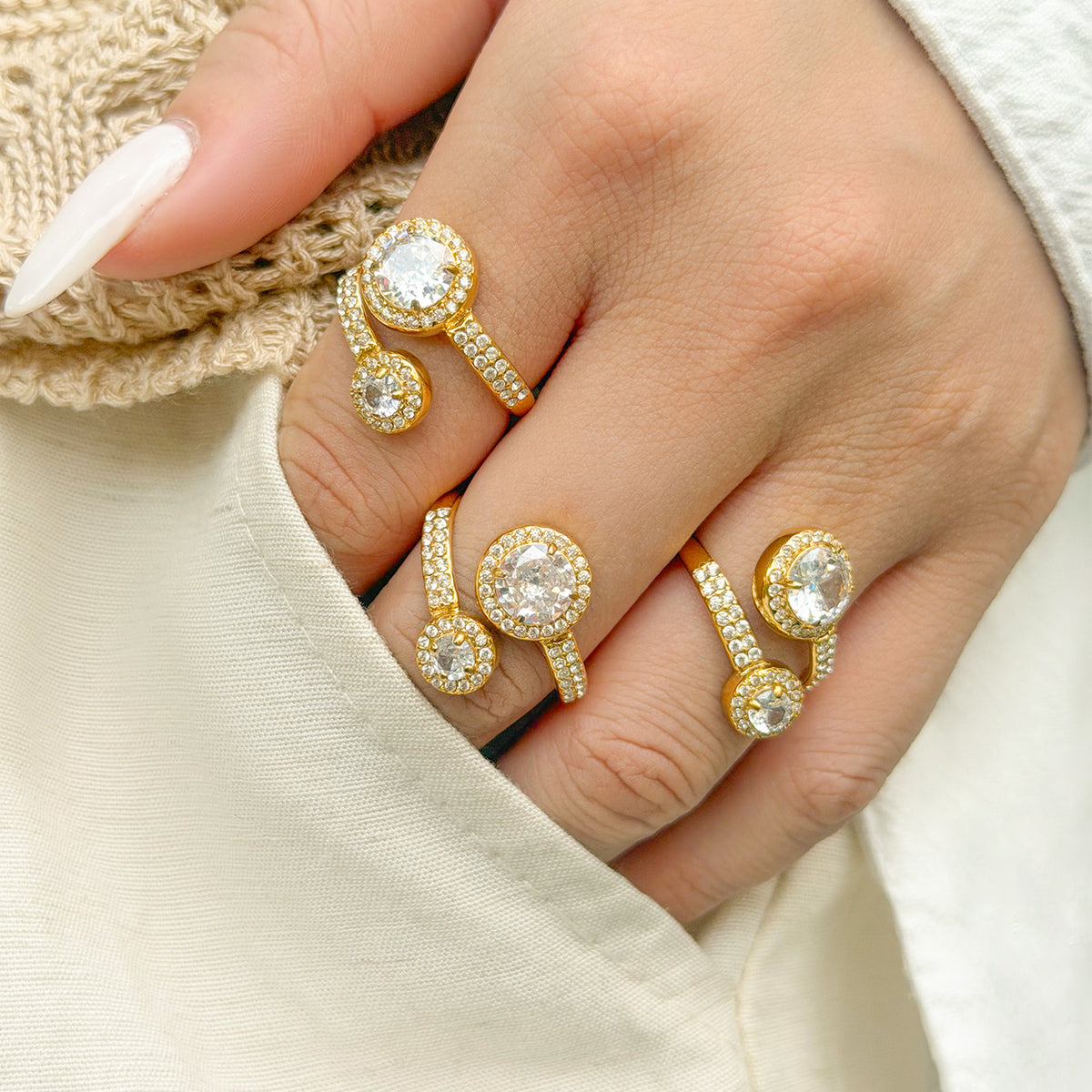 Gold-tone stainless steel double halo rings worn on a hand against white clothing