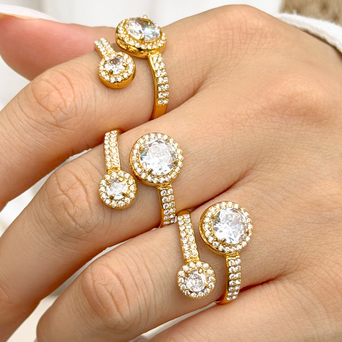 Three gold-tone stainless steel double halo rings worn on fingers, showing the large and small round stones
