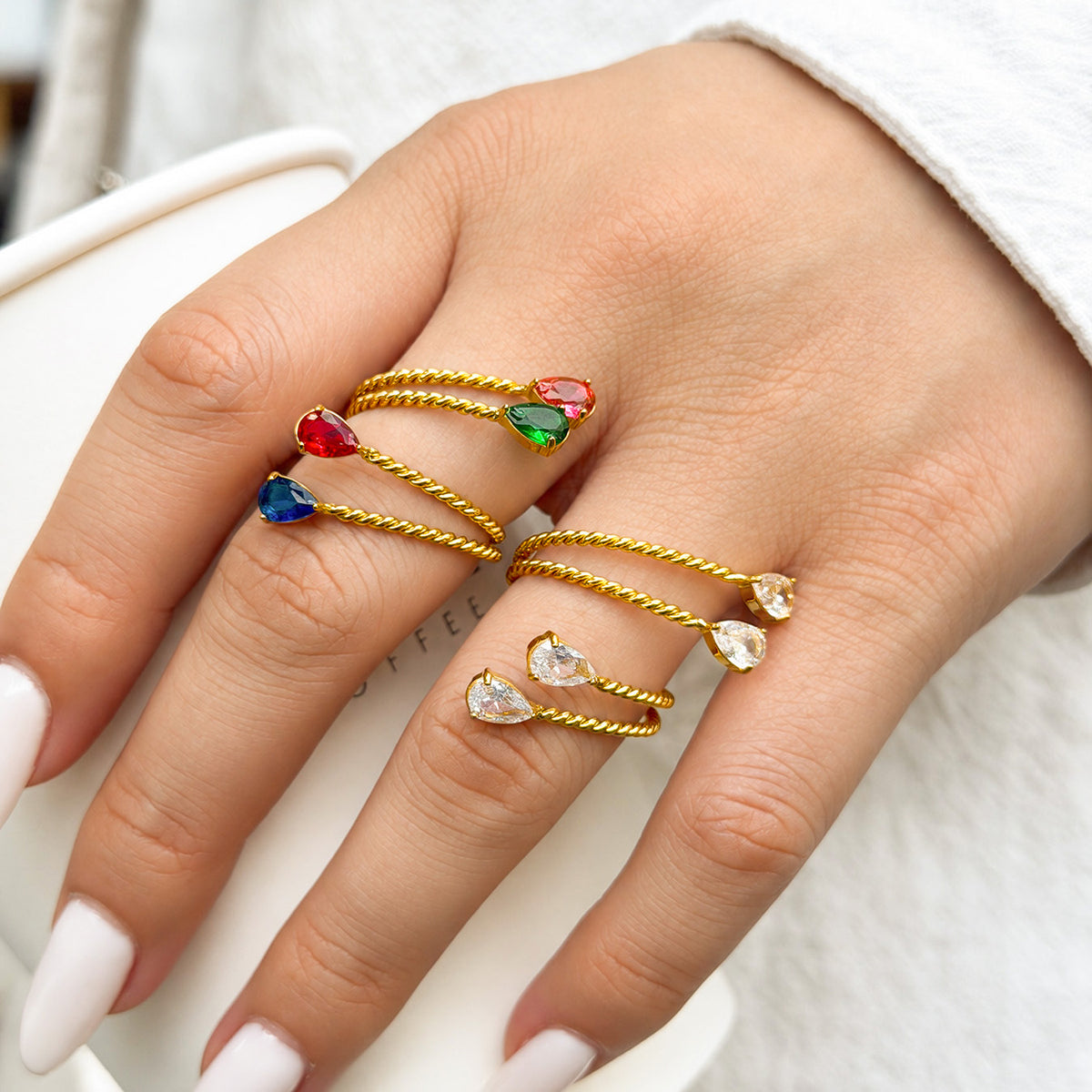 Gold-tone stainless steel twisted open rings with clear and multicolor stones worn across the fingers