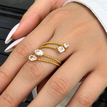 Gold-tone stainless steel twisted open rings with clear teardrop stones shown in a close-up hand styling