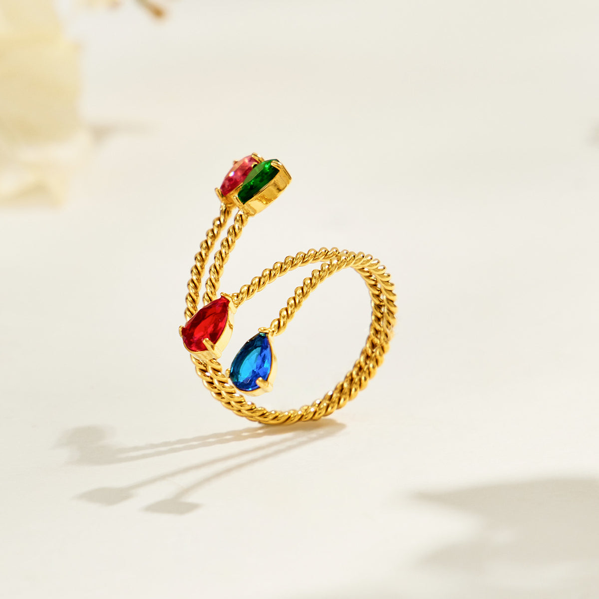 Gold-tone stainless steel twisted open ring shown at an angle with colorful teardrop stones and a rope-textured band