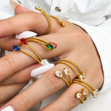 Close-up of gold-tone stainless steel twisted open rings worn on fingers with clear and colorful stone accents
