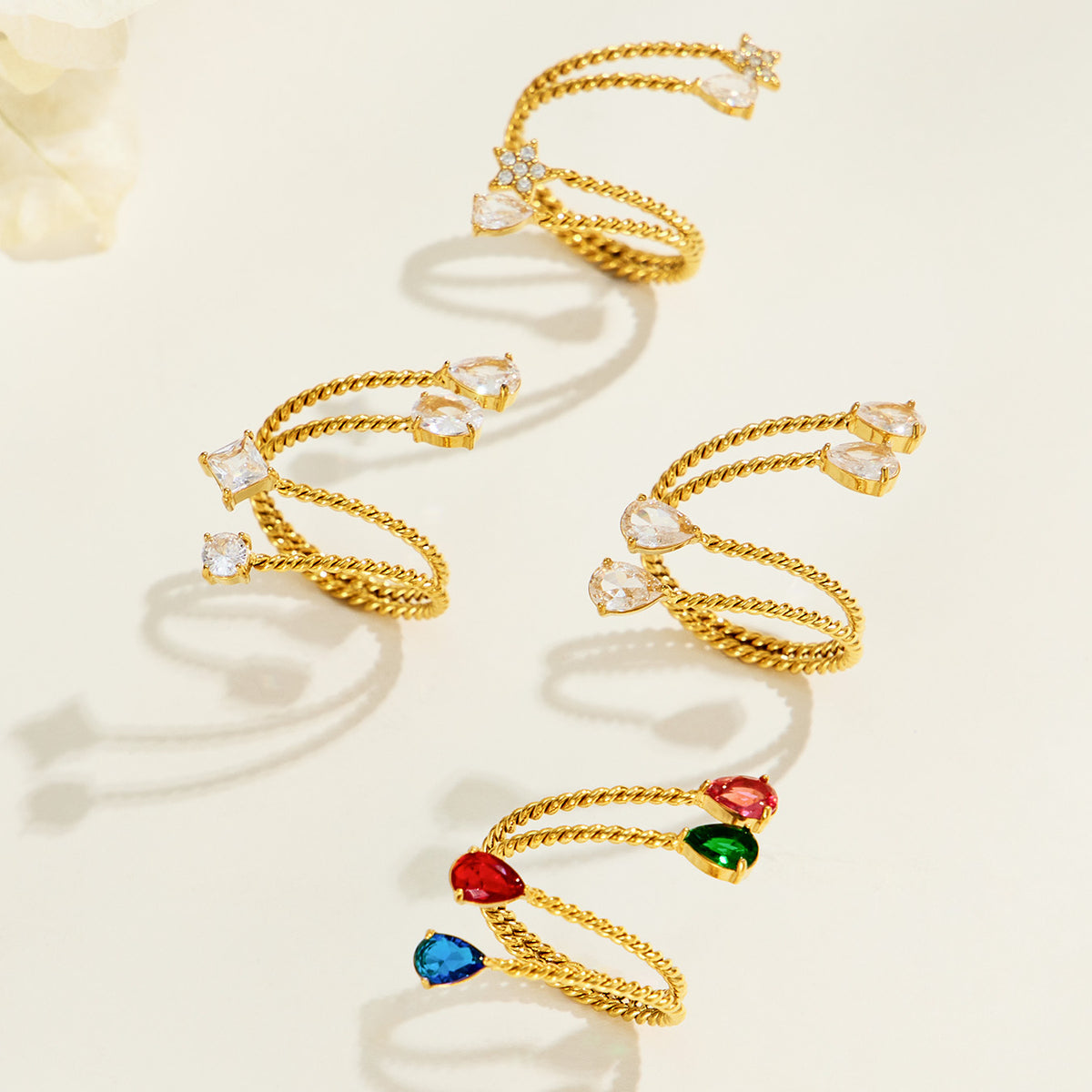 Overhead arrangement of gold-tone stainless steel twisted open rings, showing the open bands and different stone designs